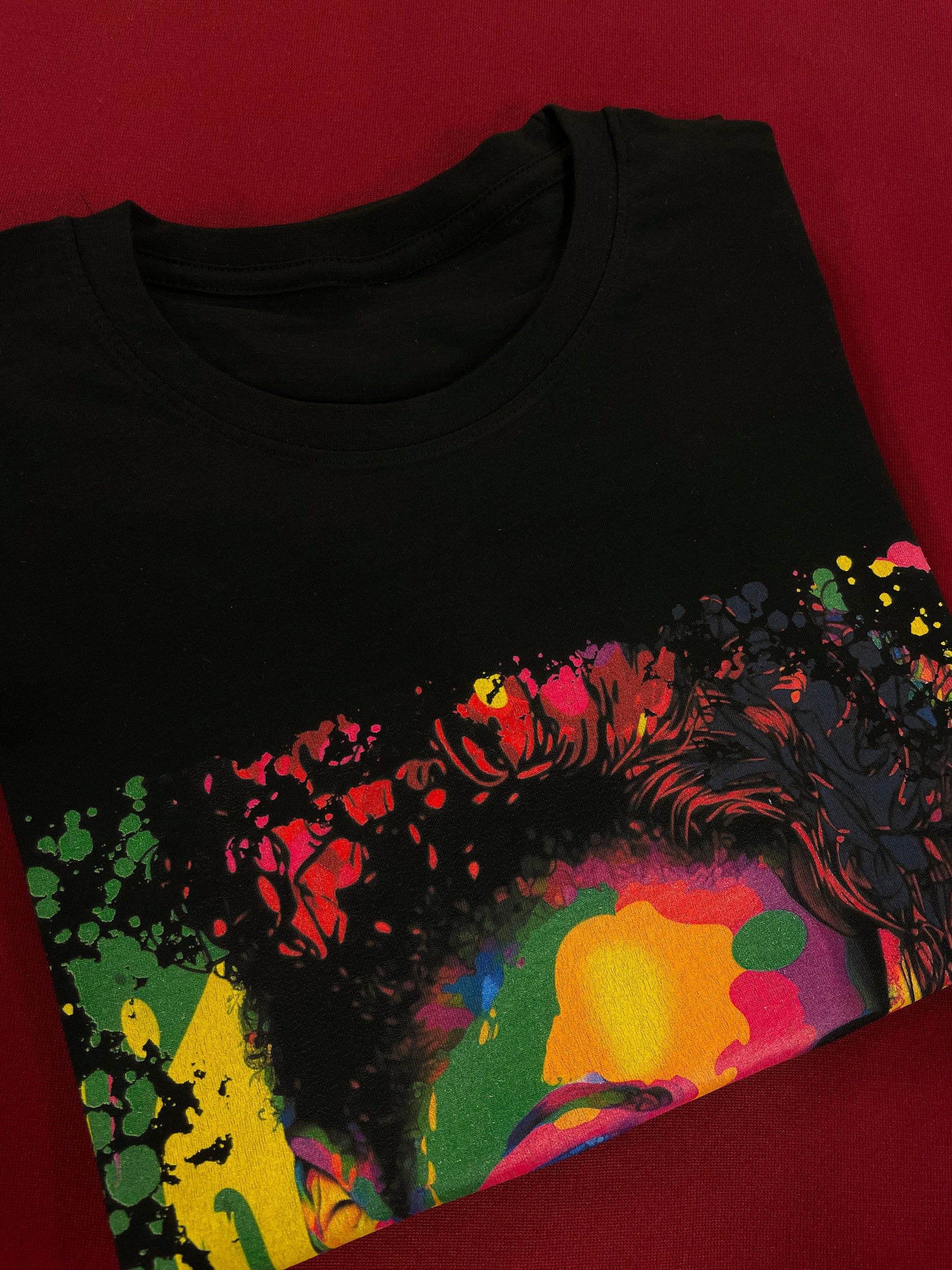 A folded unisex cotton t-shirt with a vibrant 90s pop art print, featuring bold colors and graphic shapes arranged in a playful pattern. The folded tee is shown from a top-down view, creating a neat and organized appearance.